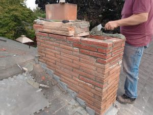 Man repairing brick chimney on roof.