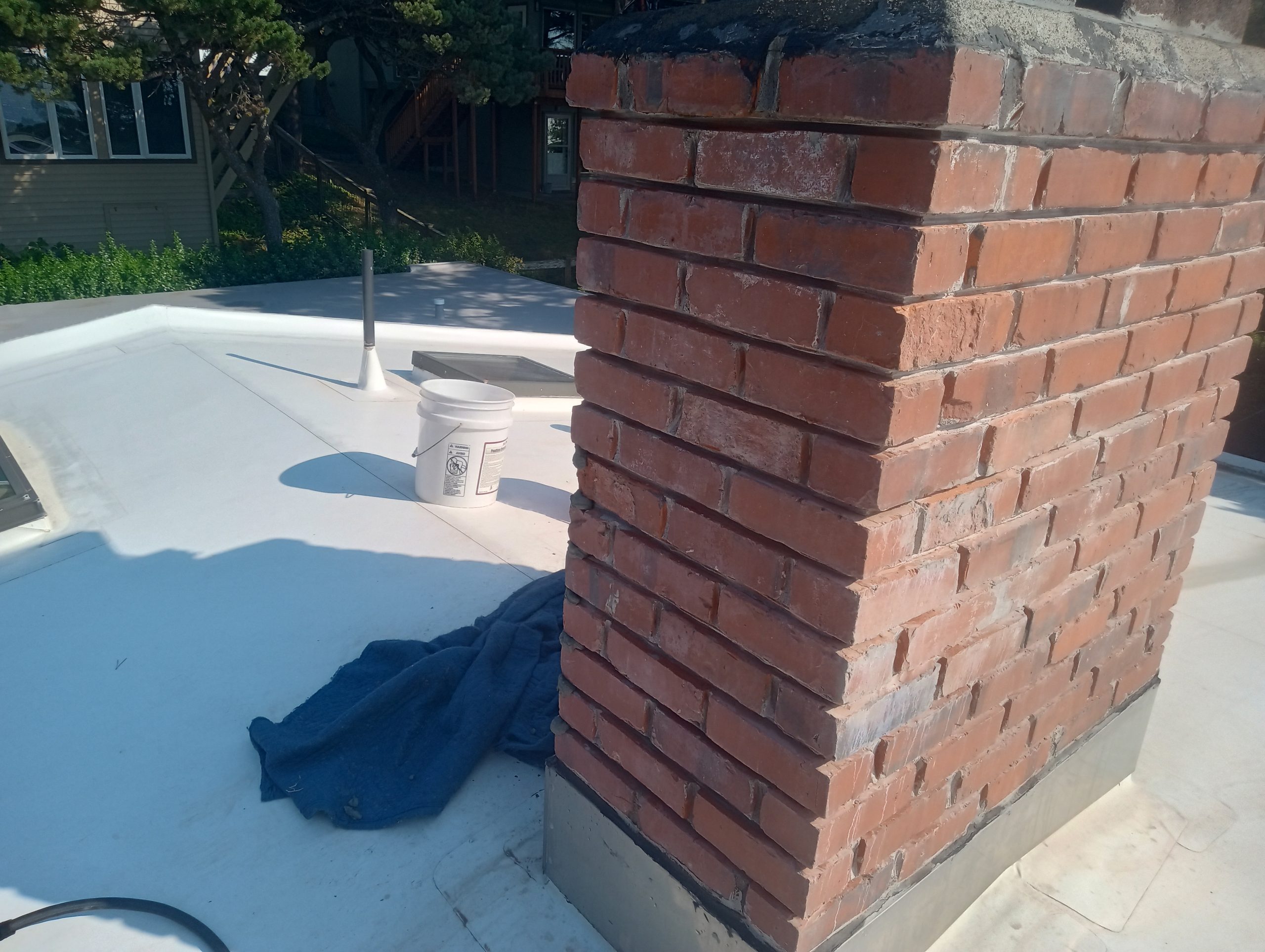 Brick chimney on flat white roof with objects. Newport Oregon home. Mortar joints have been ground out in preparation for repairs.