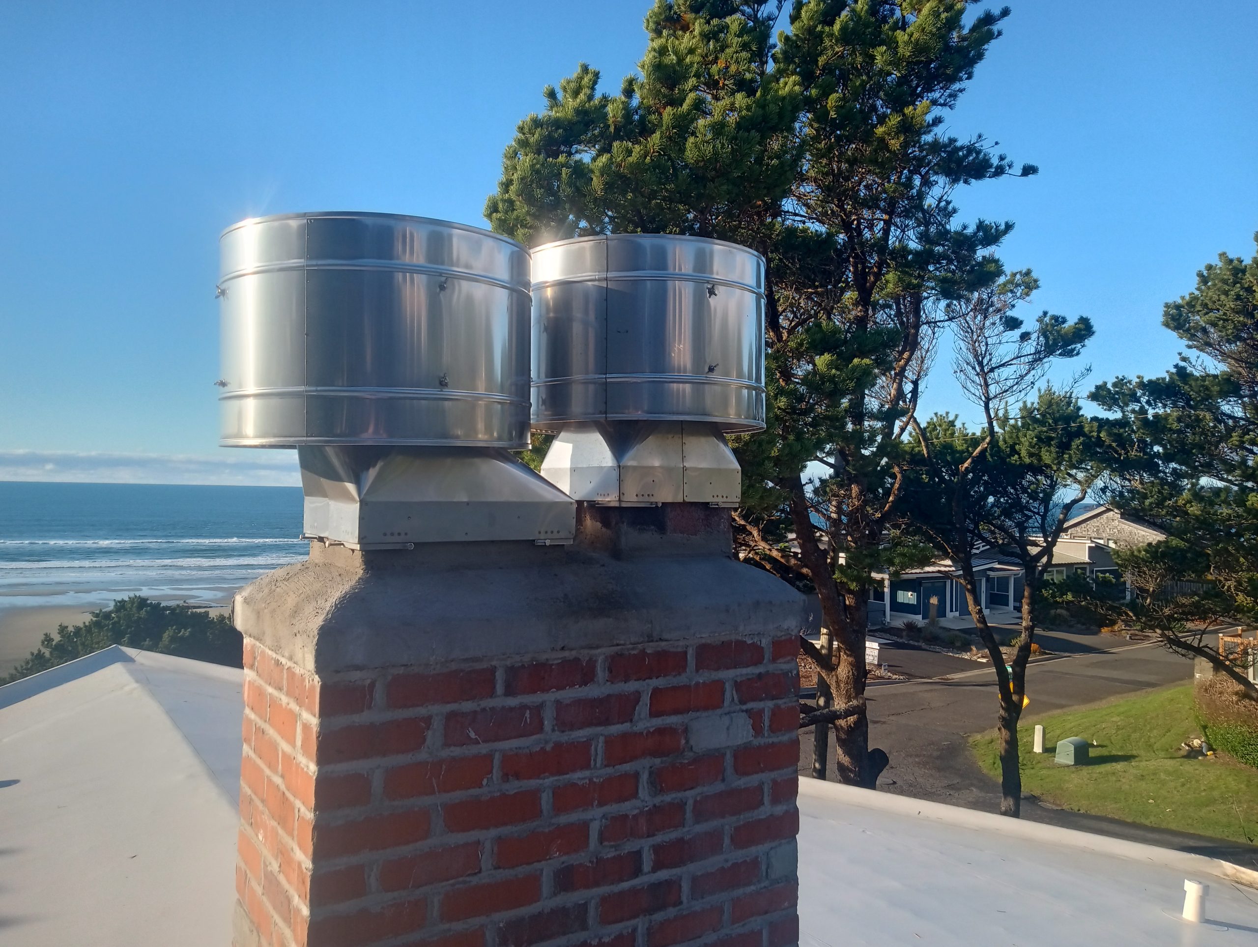 Stainless steel Monsoon rain caps installed on a chimney in Newport, Oregon. No rain can blow into the caps. Caps prevent wind downdrafts.